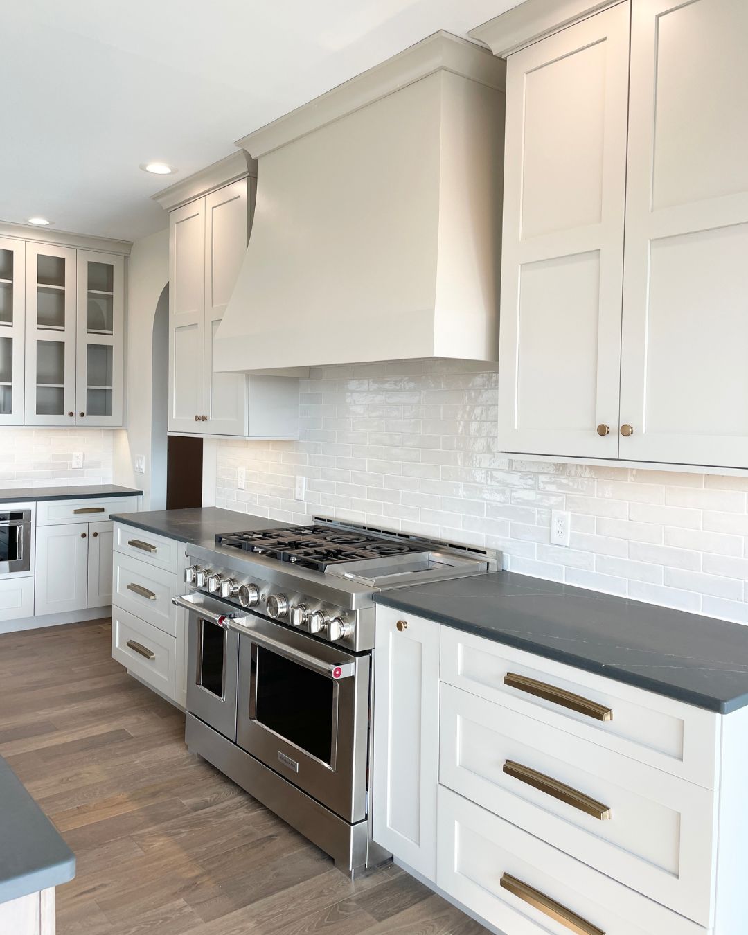 white cabinet kitchen with curved wood range hood above stainless steel commercial range