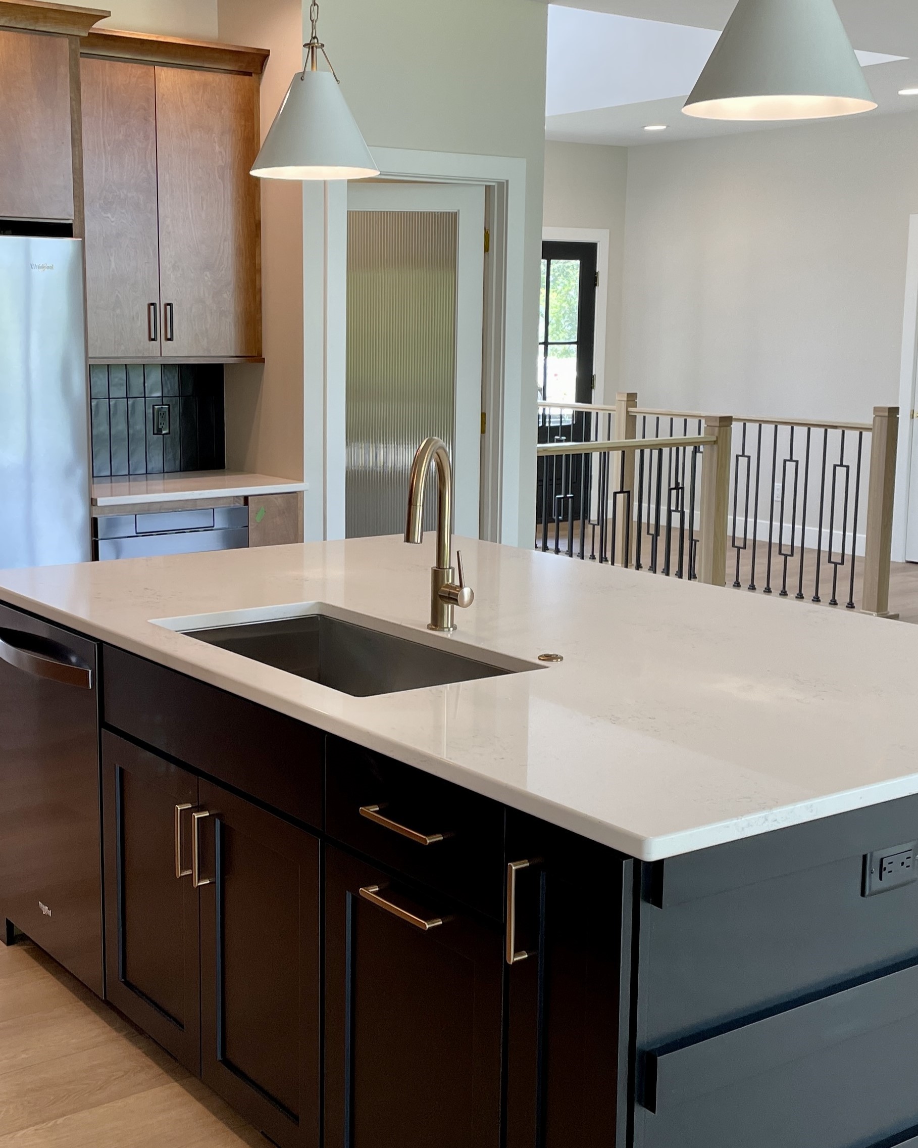 Black cabinet kitchen island with sink and brass faucet fixture. White pendant lighting above