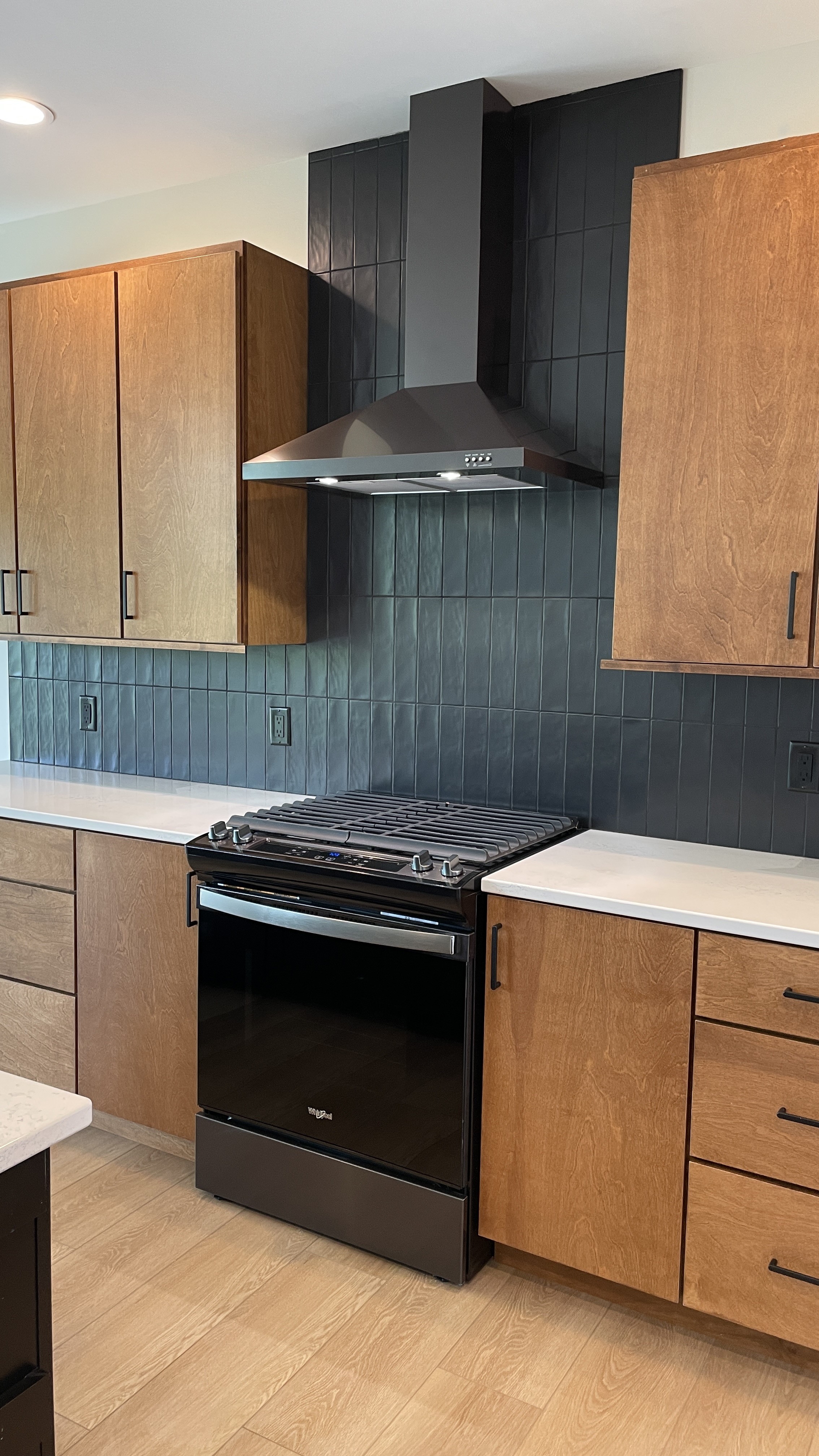 medium stained birch cabinetry in a contemporary kitchen with black stainless steel chimney hood and gas range