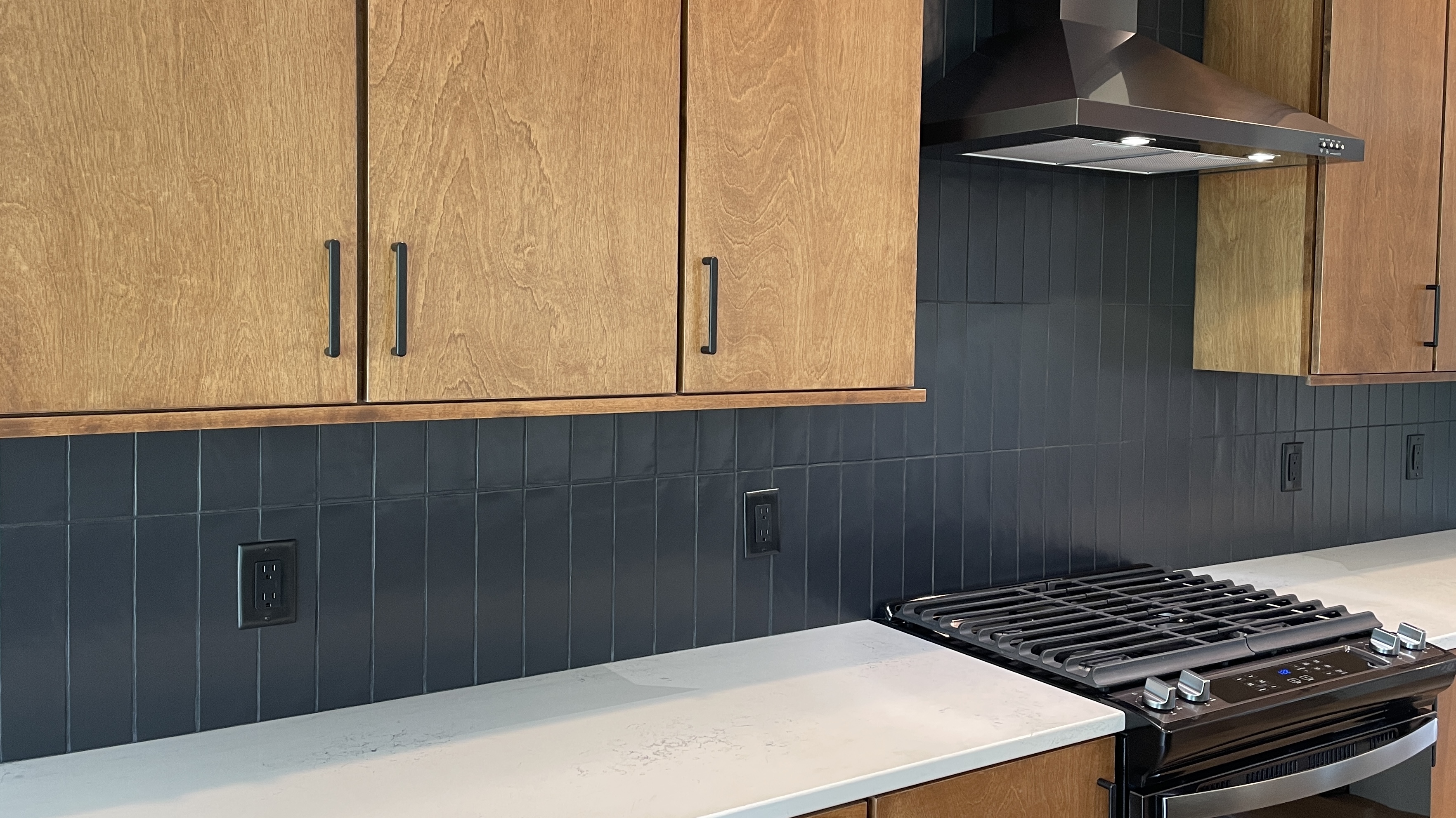 slab style cabinet kitchen with medium wood stain and black subway tile installed in a vertical stack