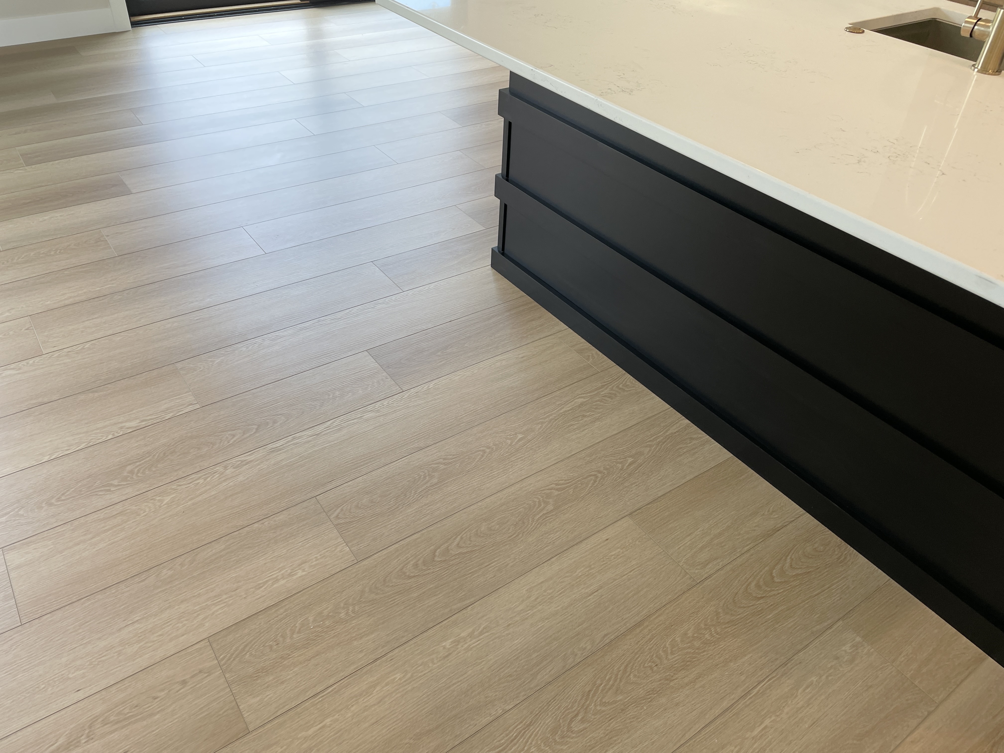 back corner of black painted kitchen island set on light white oak flooring in open concept kitchen
