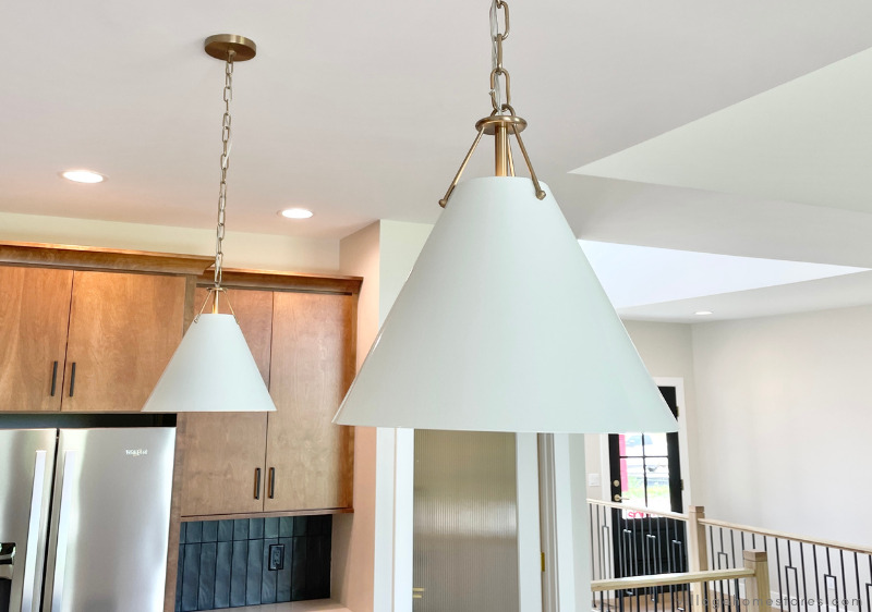 a pair of white and brass pendant lights hanging above a kitchen island