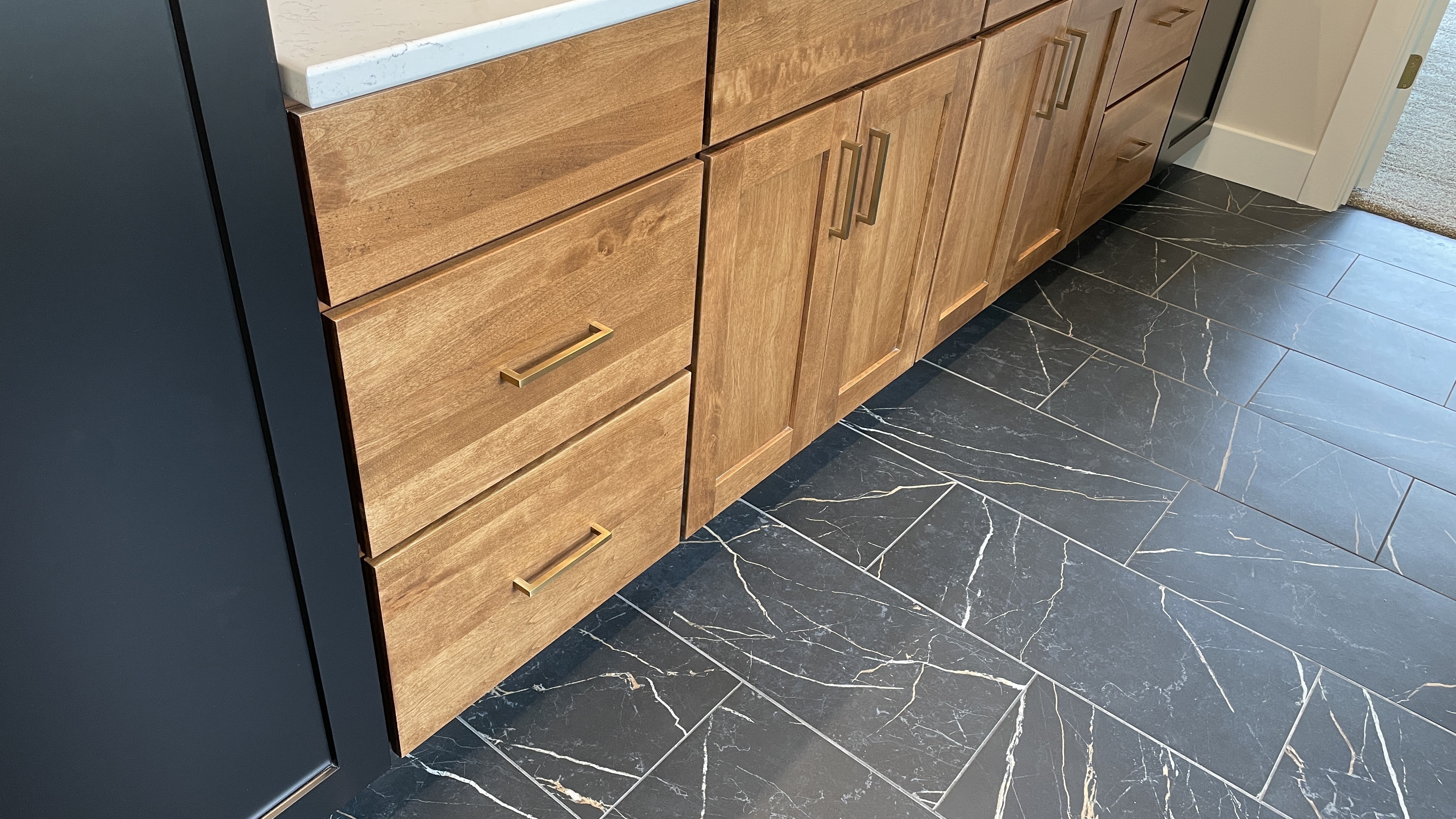birch and black painted bathroom vanity cabinets with brass handle hardware on black marble patterned tile floors
