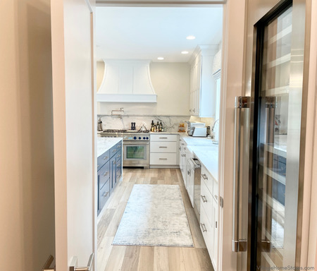 view of bright white kitchen design looking out through doorway of walk-in pantry