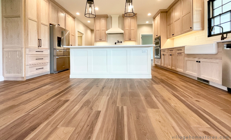 wide shot from floor of wood look vinyl plank floors in kitchen with light oak wood cabinets and painted white island