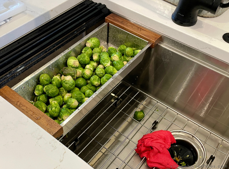 overhead view of stainless steel workstation style kitchen sink with colander filled with Brussel sprouts 