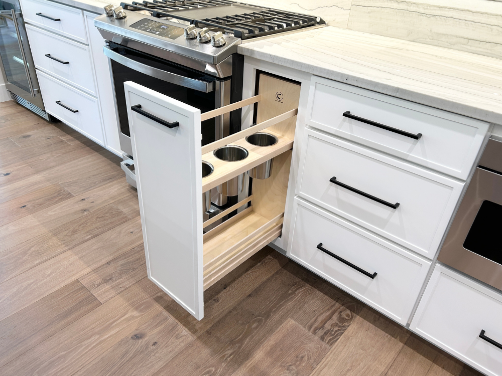 painted frost white base cabinet by range open showing utensil pullout storage cabinet with stainless utensil caddies