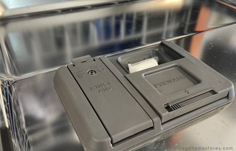 white dishwasher pod placed in gray plastic dispenser of dishwasher door 