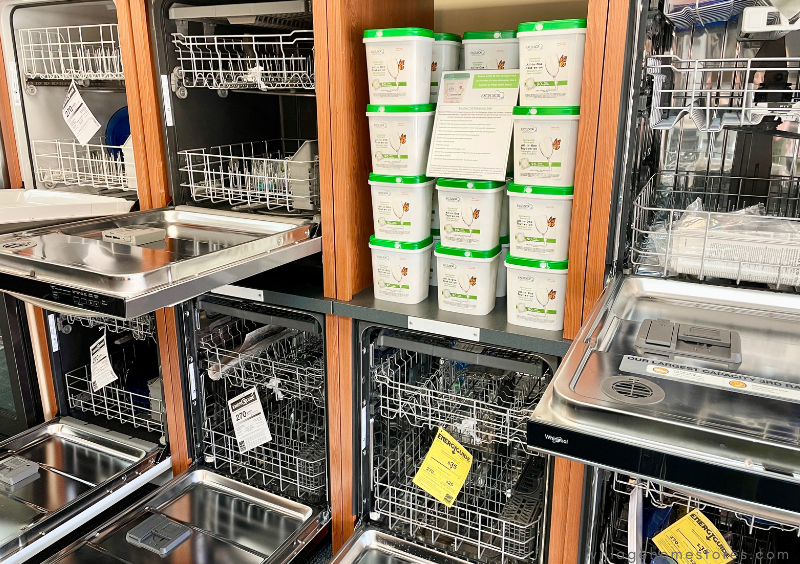 appliance showroom dishwasher display with stacked bins of dishwasher pods