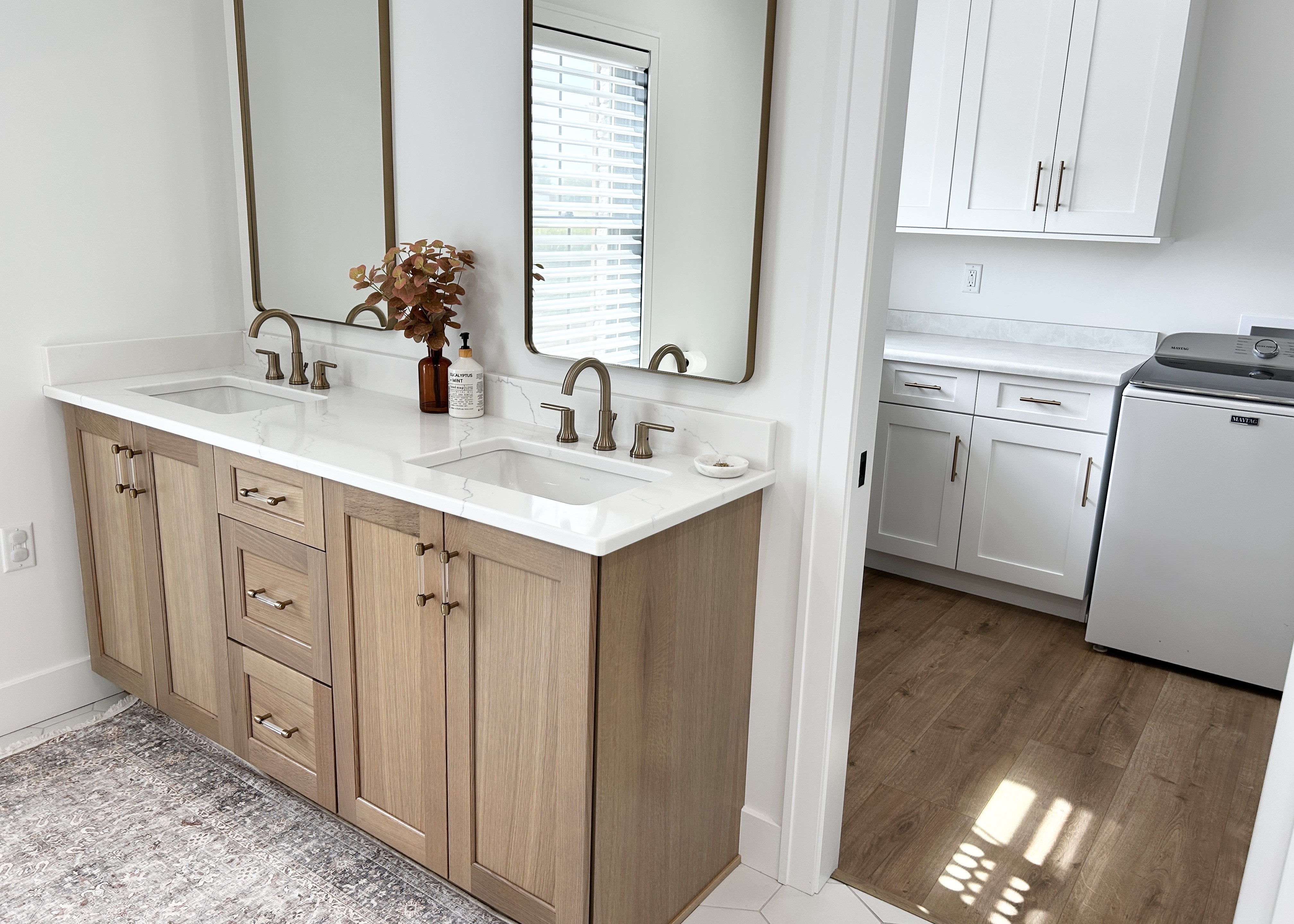 light white oak double sink vanity and look into white cabinet laundry room of primary suite