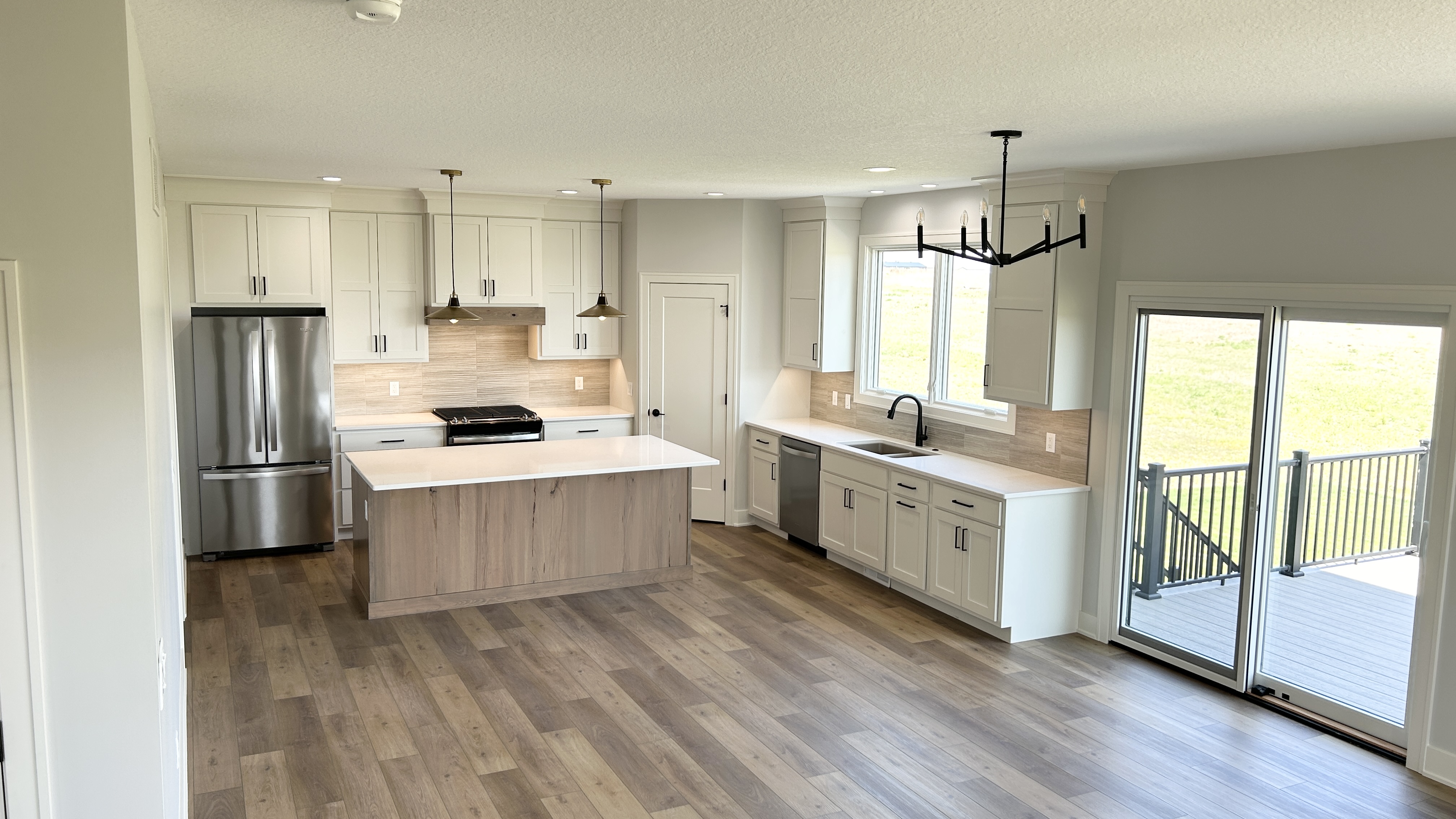 White and medium wood great room kitchen design with large single-level island and stainless appliances. Village Home Stores kitchen for Wood Builders in a new LeClaire, Iowa home. 