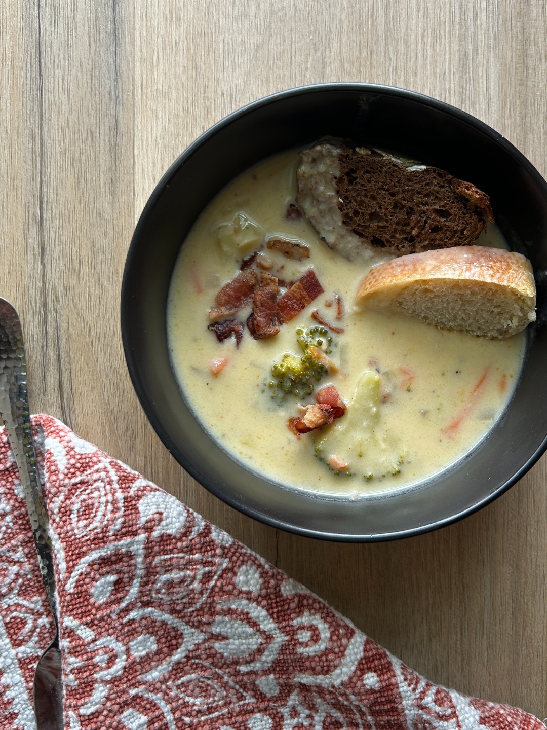 black bowl with broccoli cheddar soup garnished with bread and bacon