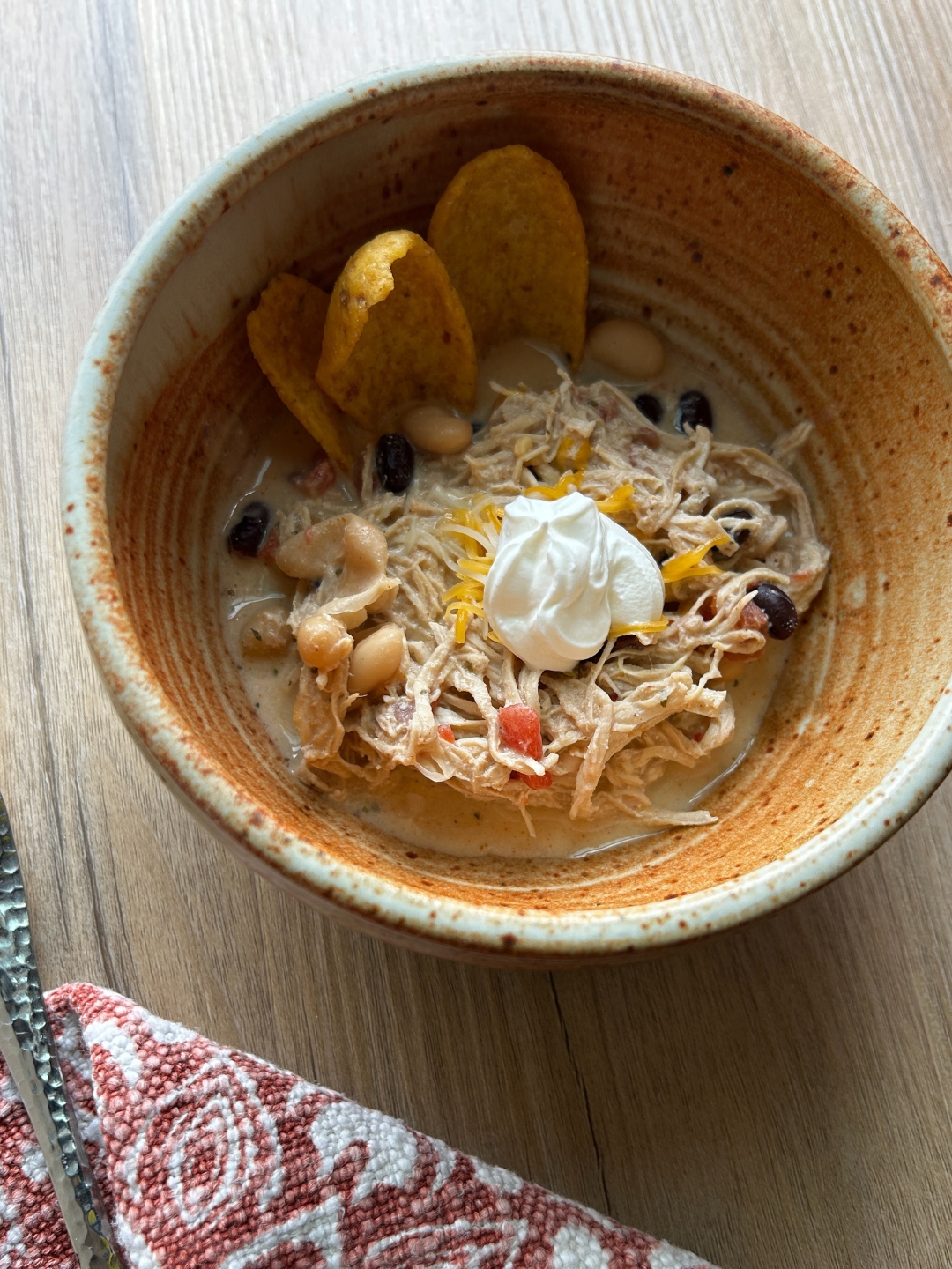 bowl of white chicken chili garnished with fritos scoops sour cream and shredded cheese