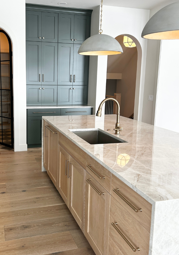light oak kitchen island in white oak sand with waterfall taj mahal countertops and green painted cabinets in the background