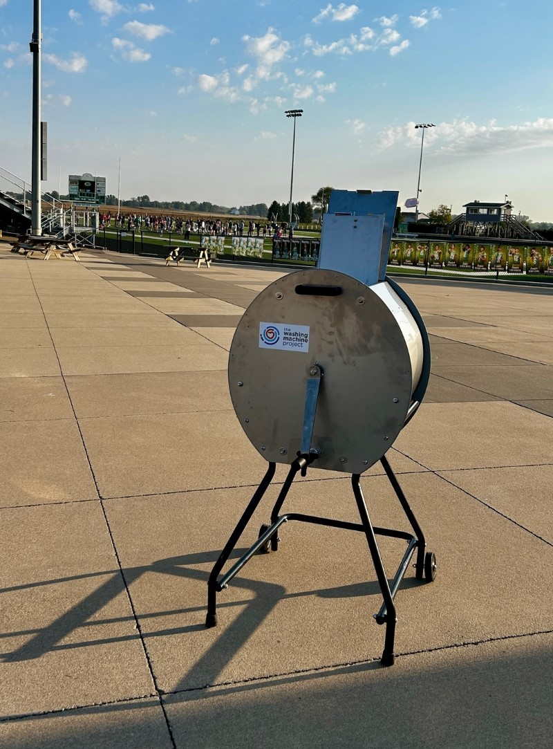 divya manual washing machine at Geneseo high school football field with band practicing in background