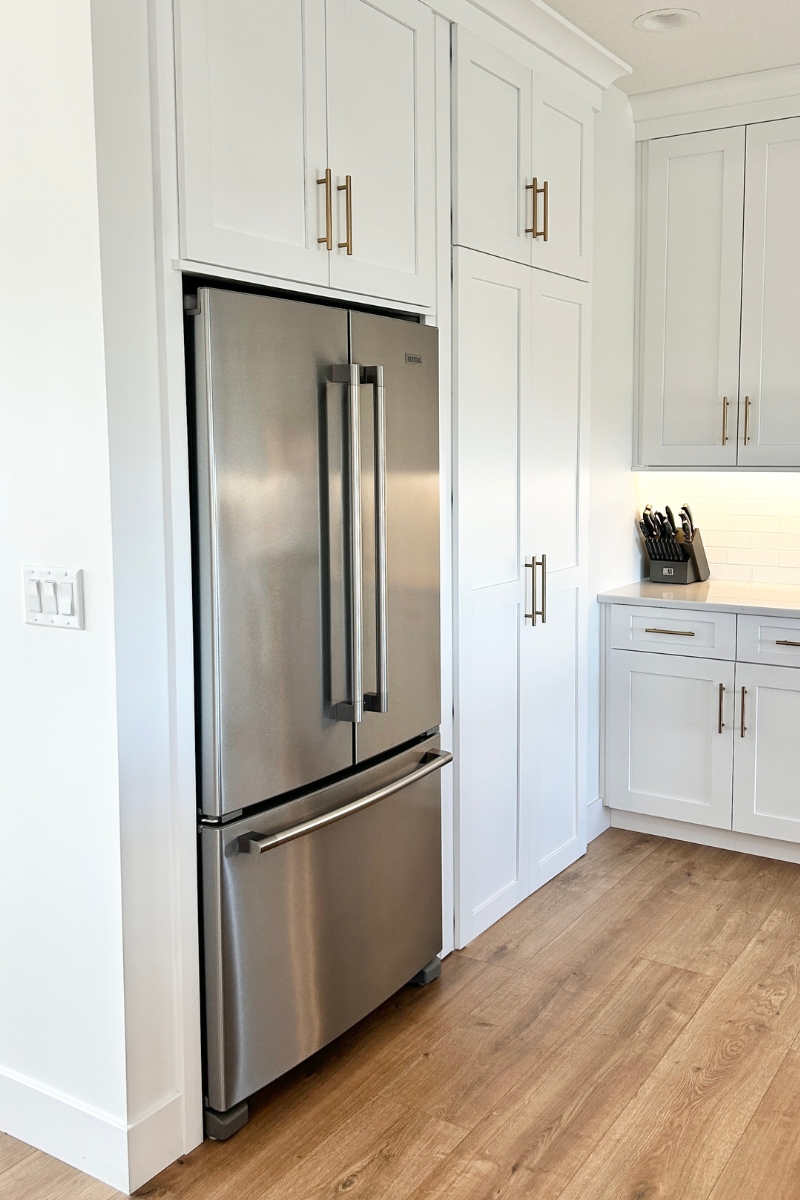 maytag French door stainless steel refrigerator shown built into wall recess with cabinet above and pantry doors to right