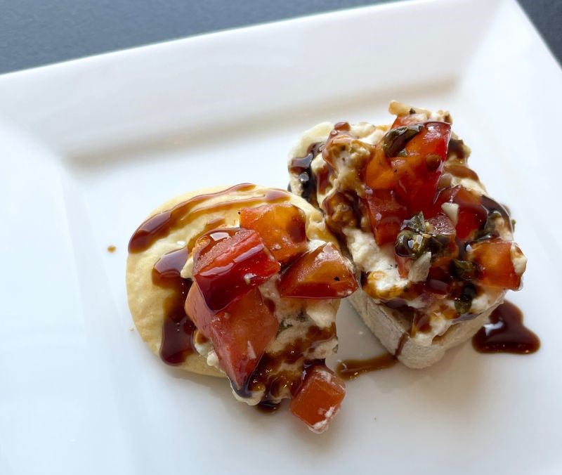white square plate with bread and pita chip layered with bruschetta goat cheese dip and balsamic glaze