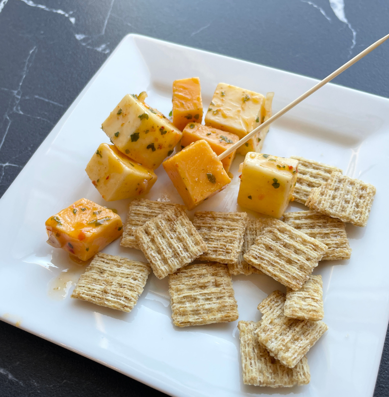 white square plate with small Triscuit crackers and cheese cubes with spicy marinade 