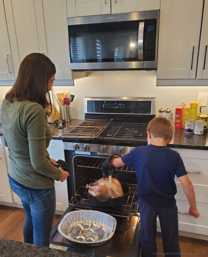 mother and son with oven door open shown basting a turkey in whirlpool oven