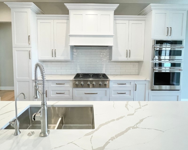 white cabinet kitchen with white quartz island top and sink with faucet and disposal button