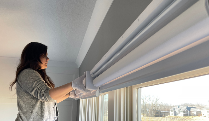 woman with grey shirt and brown hair installing window valance