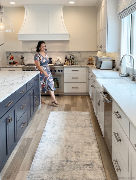 women in blue floral dress walking around blue cabinet kitchen island towards white farm sink