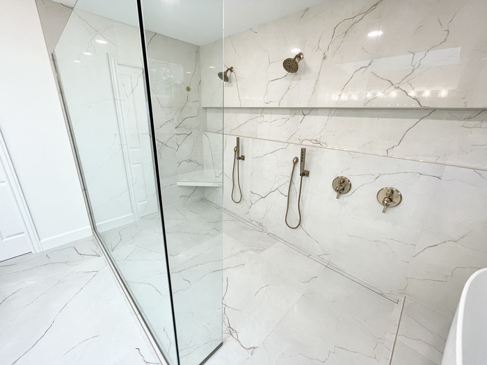 large tiled shower with double shower heads and controls and glass panels