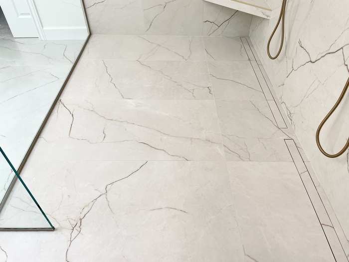image of slanted tiled shower floor with large sized tiles and set of linear tiled drains