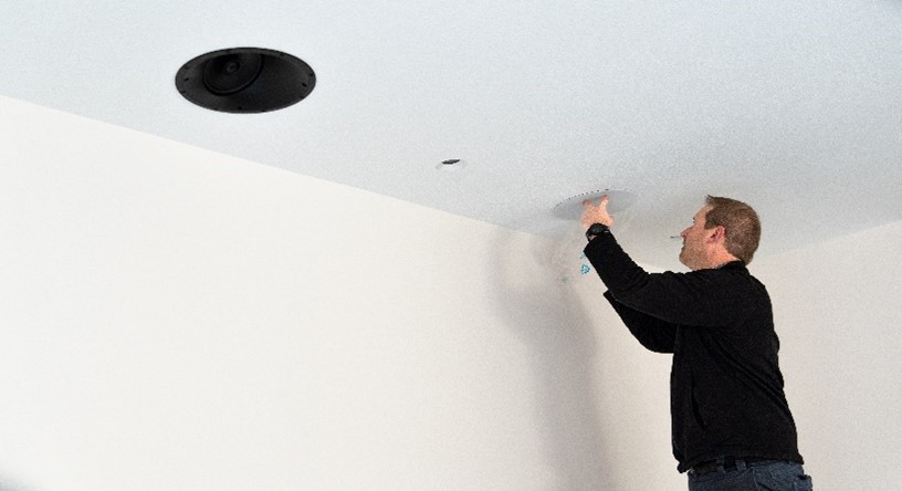 A technician installs speakers in the ceiling of a home. 