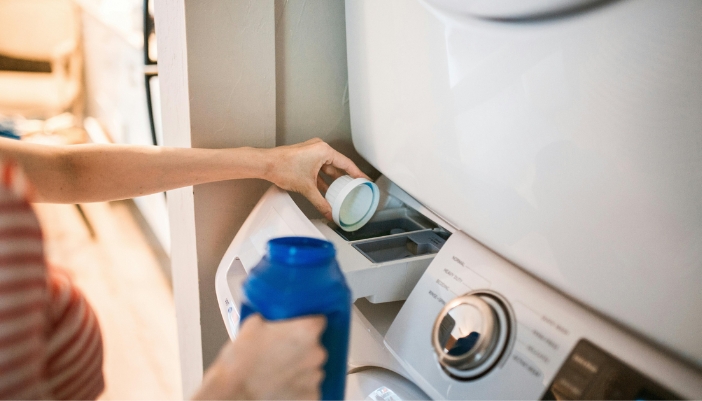 A female hand loads detergent into a washing machine.