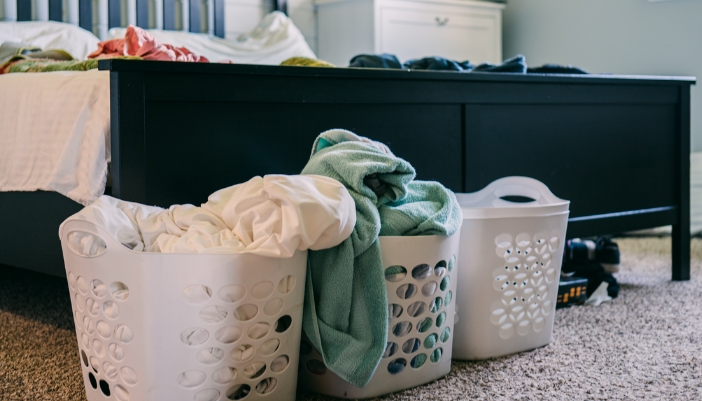 A close-up of the end of a laundry covered bed with full baskets on the floor.
