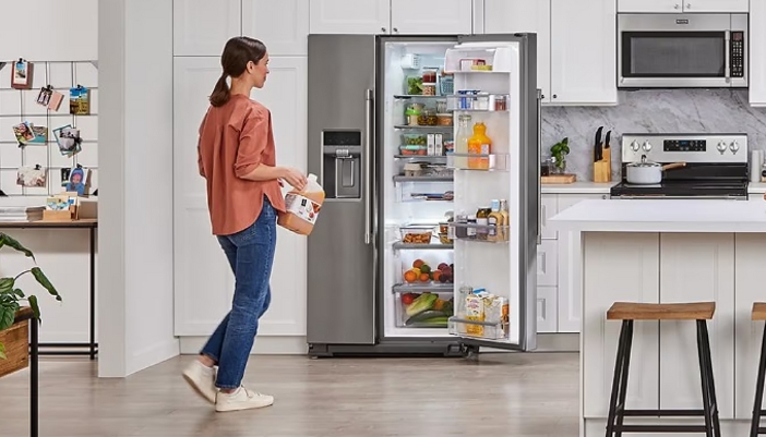 A woman loads a juice bottle back into her full fridge.