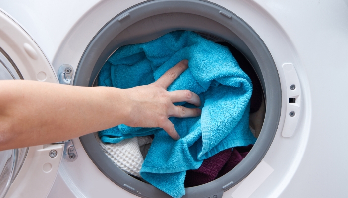 A hand puts a blue towel into a washing machine.
