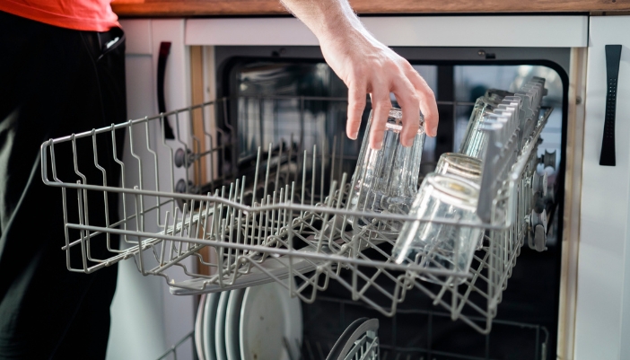 A female hand loads a dishwasher at home.