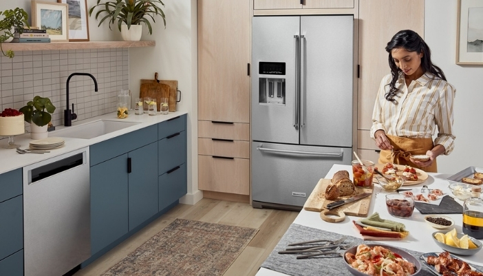 A woman prepares a meal beside a French-door refrigerator in her kitchen. 