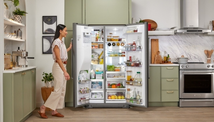 A woman in a green kitchen looks through her side-by-side refrigerator