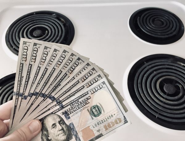 A person fanning $100 bills over an electric coil stove 