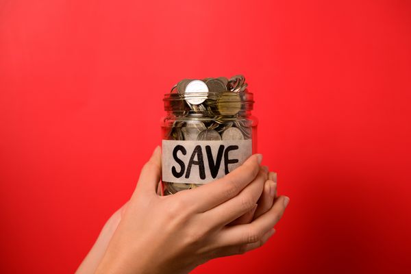 A person holding a jar of coins with a save sticker in front of a red background  