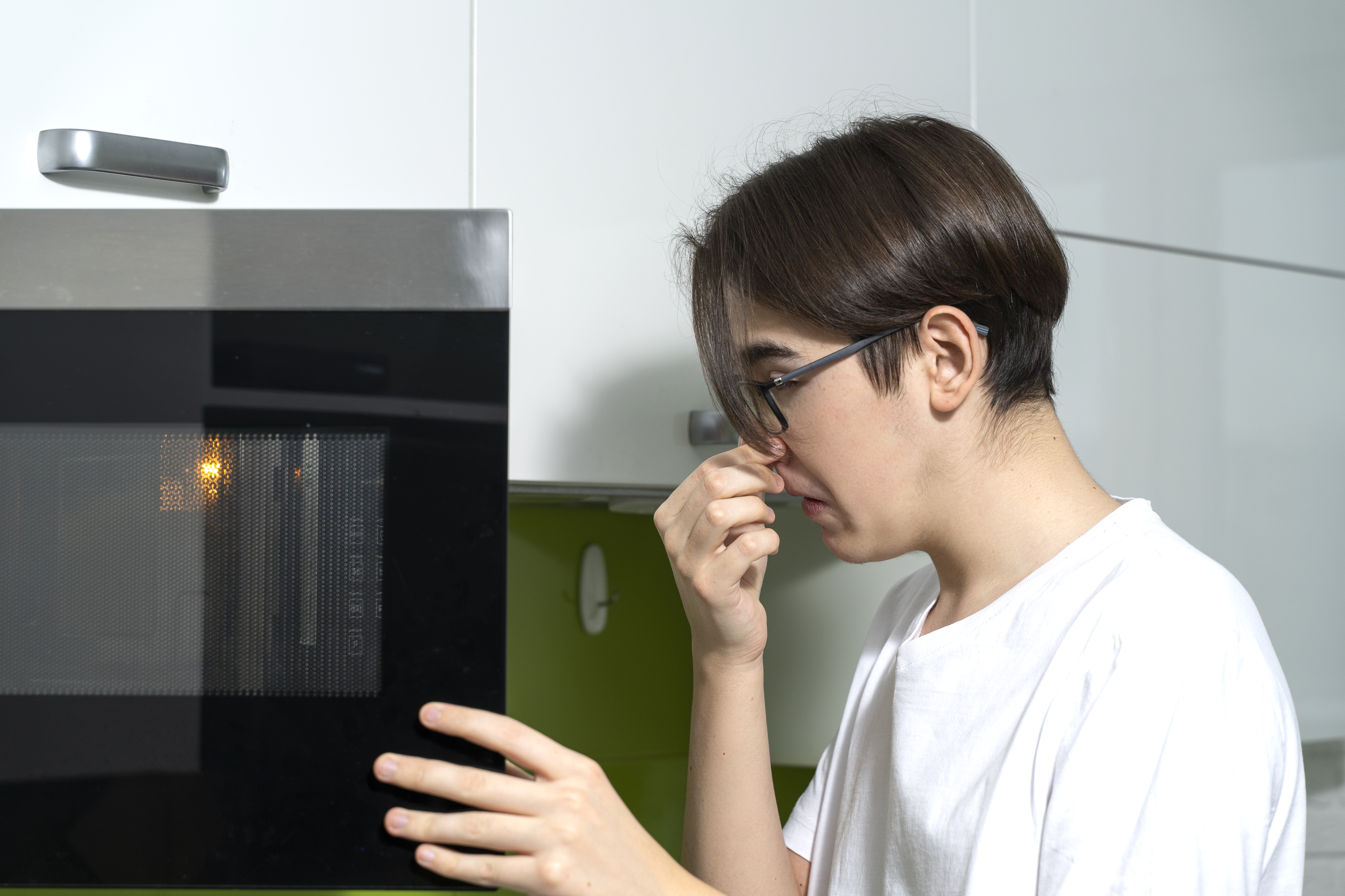 A young man holding his nose while opening a microwave 