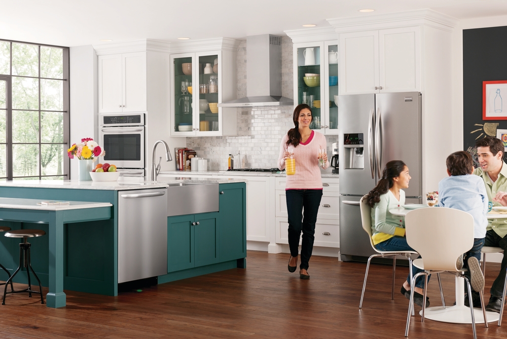Mother walking towards family eating at table in modern kitchen with frigidaire gallery stainless steel appliances