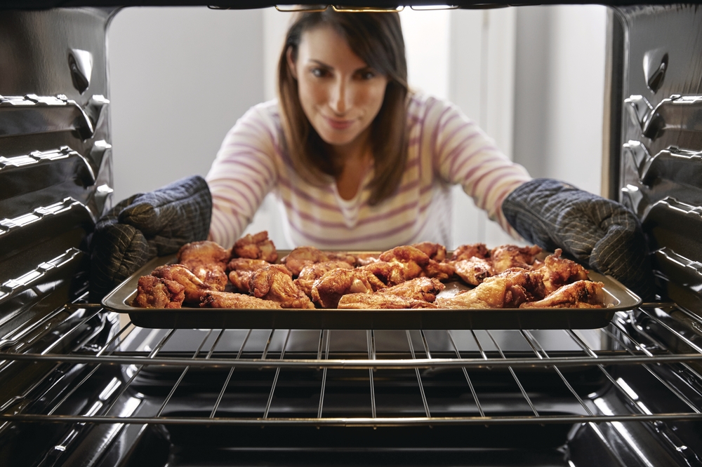 Shot from inside a Frigidaire wall oven of woman retrieving chicken wings