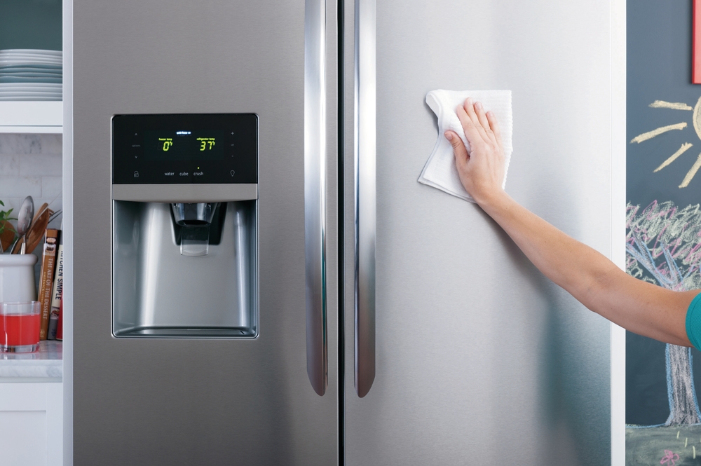 woman cleaning frigidaire gallery stainless steel side by side refrigerator with smudge-proof finish