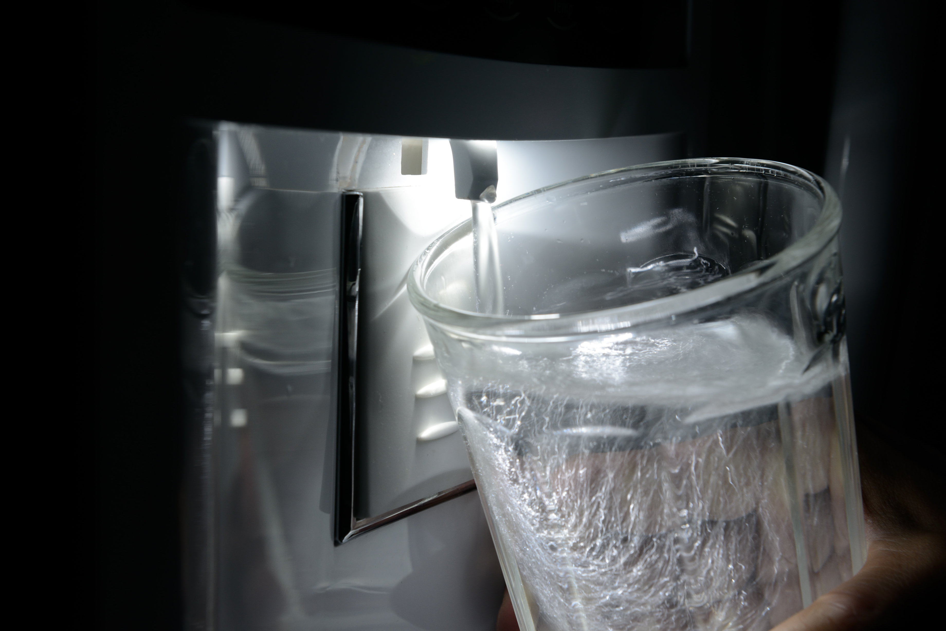 Closeup of refrigerator water dispenser dispensing water into a glass
