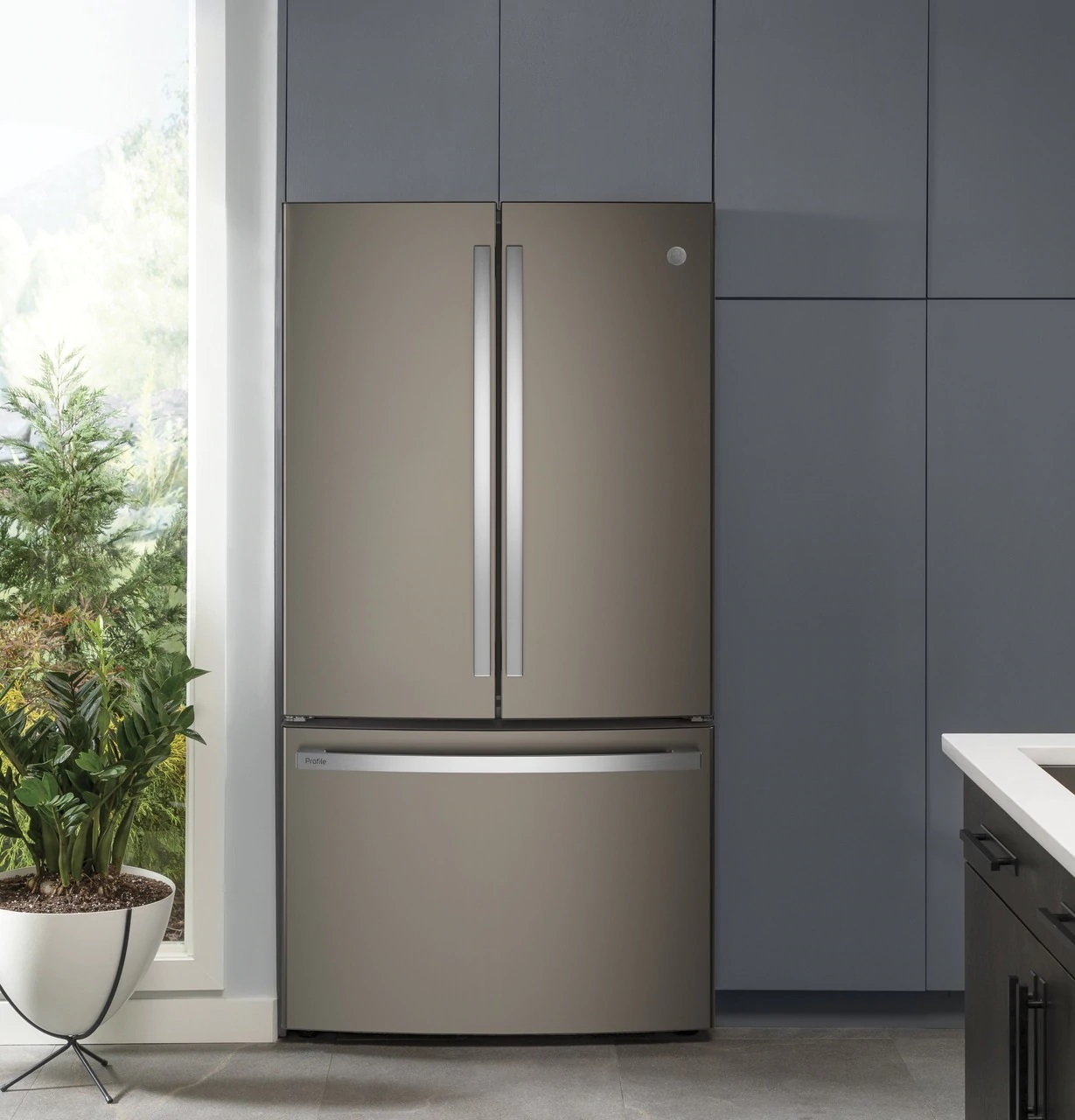 ge profile PWE23KMKES French door fridge in a modern grey kitchen with plants 