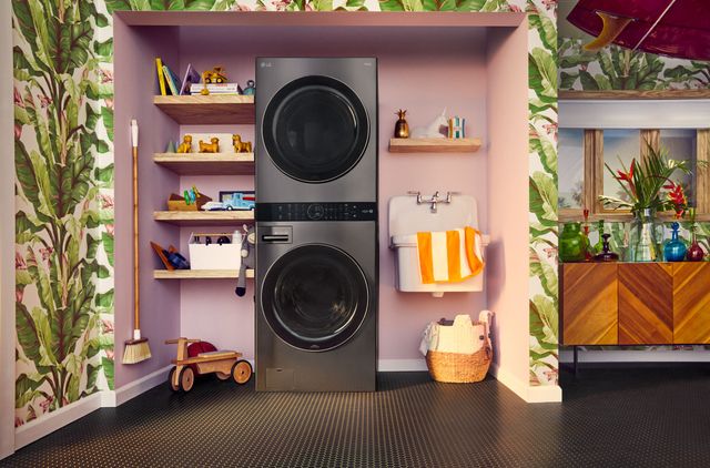 front view of a modern laundry room with an lg washtower and a sink in a built in wall storage feature made of light gray wood on a white tile backsplash