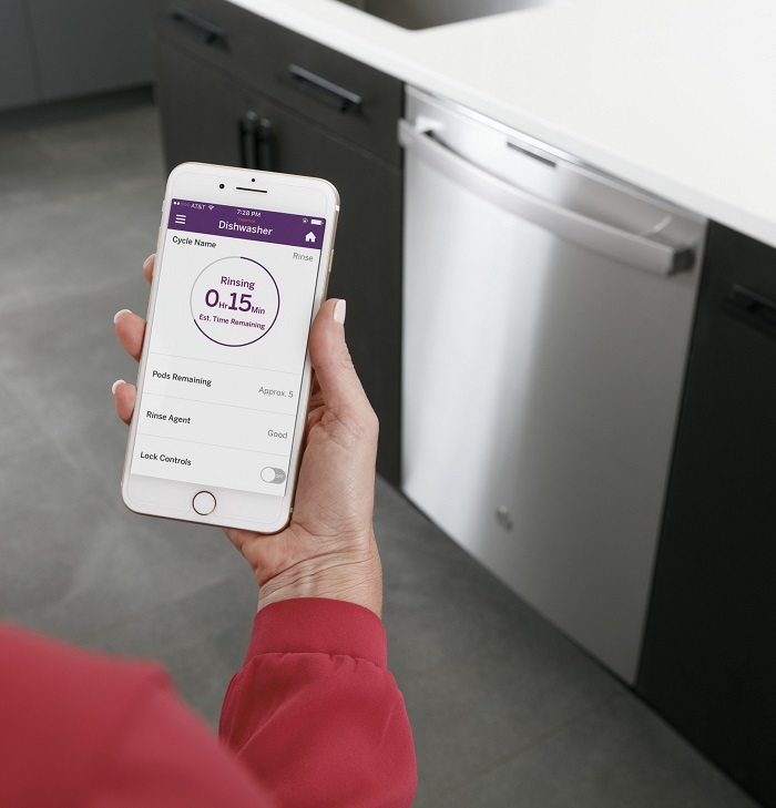 Woman standing with smartphone next to dishwasher.