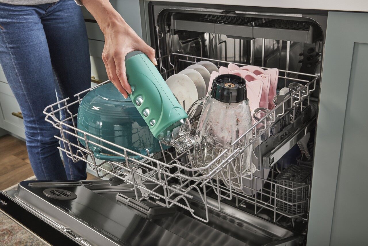 User loading a tall water bottle into Whirlpool WDT750SAKZ middle rack 