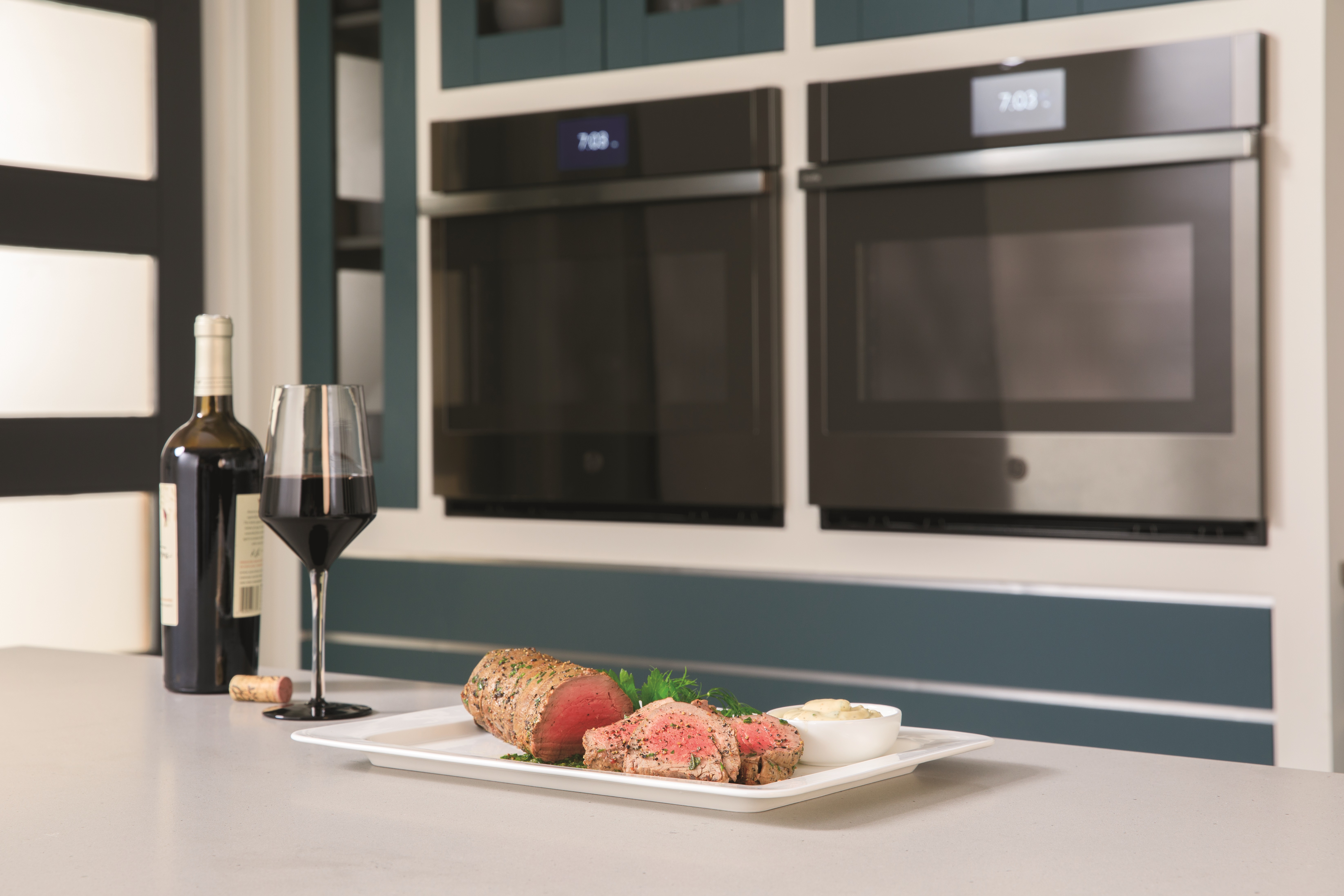 Platter of roast beef and a glass of wine staged in front of GE Profile wall ovens 