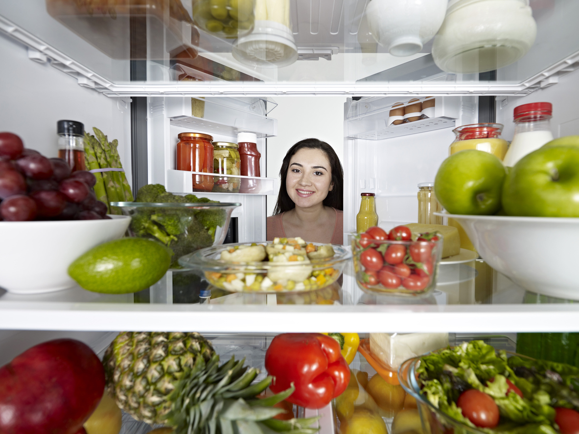 internal shot of woman looking into refrigerator full of fresh produce