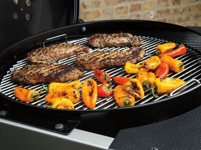 Close view of steaks and peppers being cooked on a Weber charcoal grill